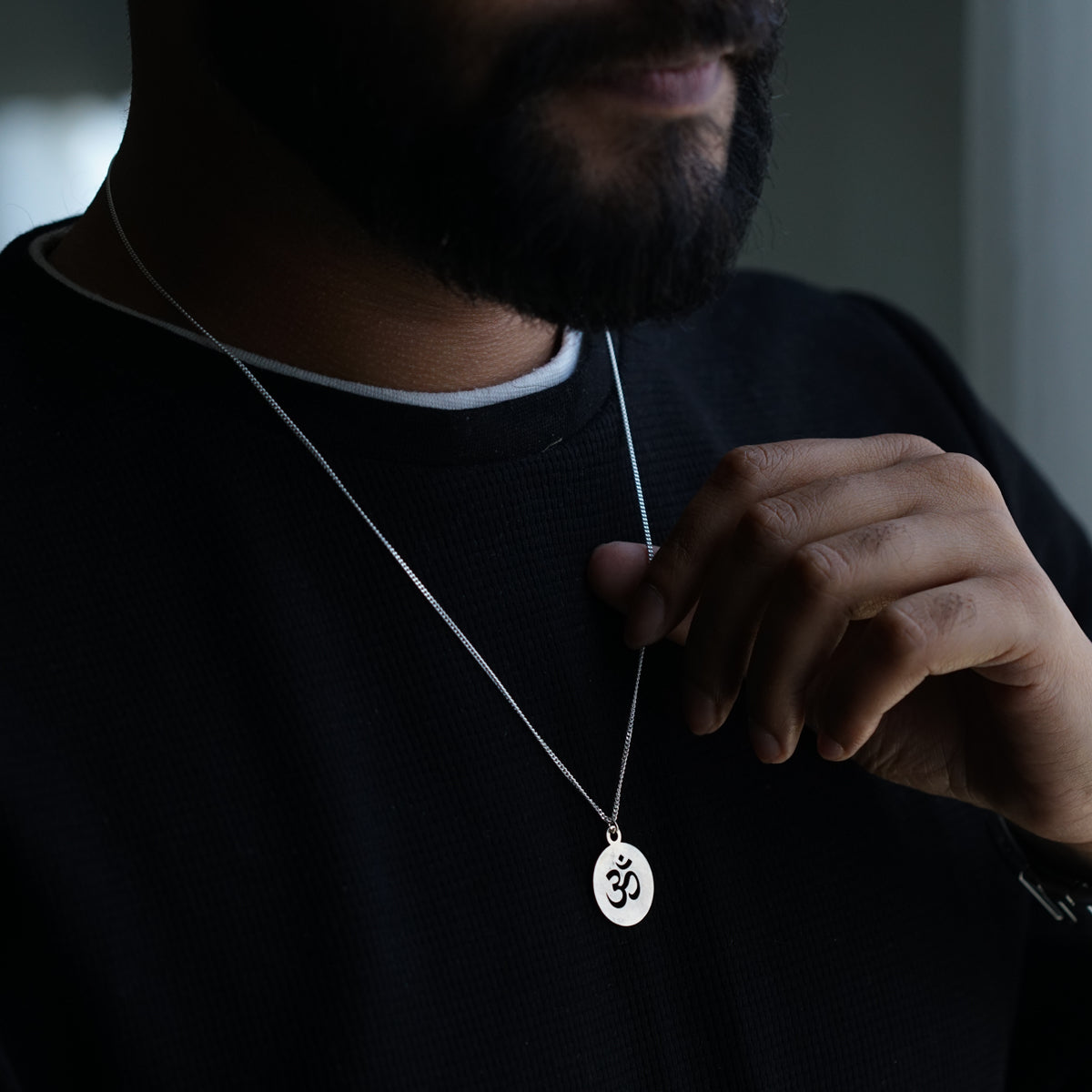 a man wearing a necklace with a small pendant on it
