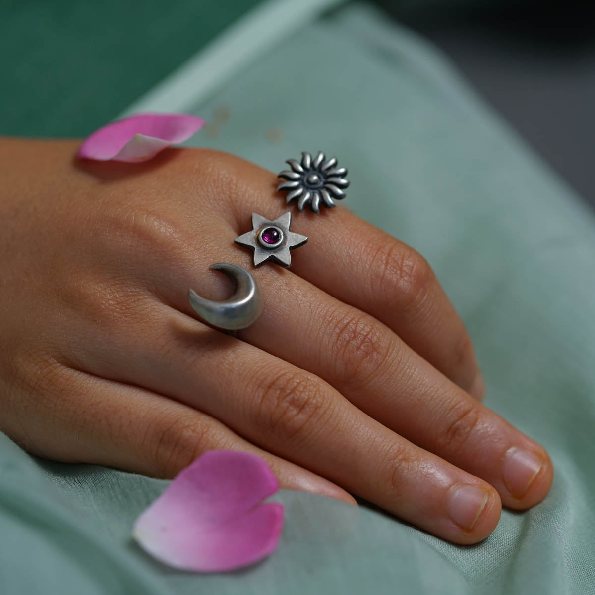Silver moon, star, and sun rings on finger with pink flower petals