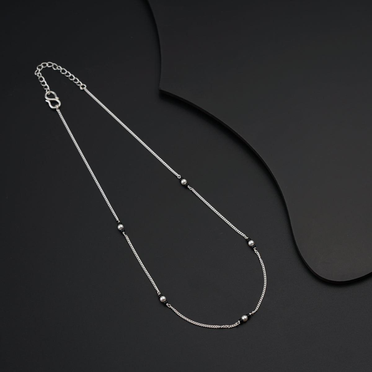 a silver necklace with beads on a black background
