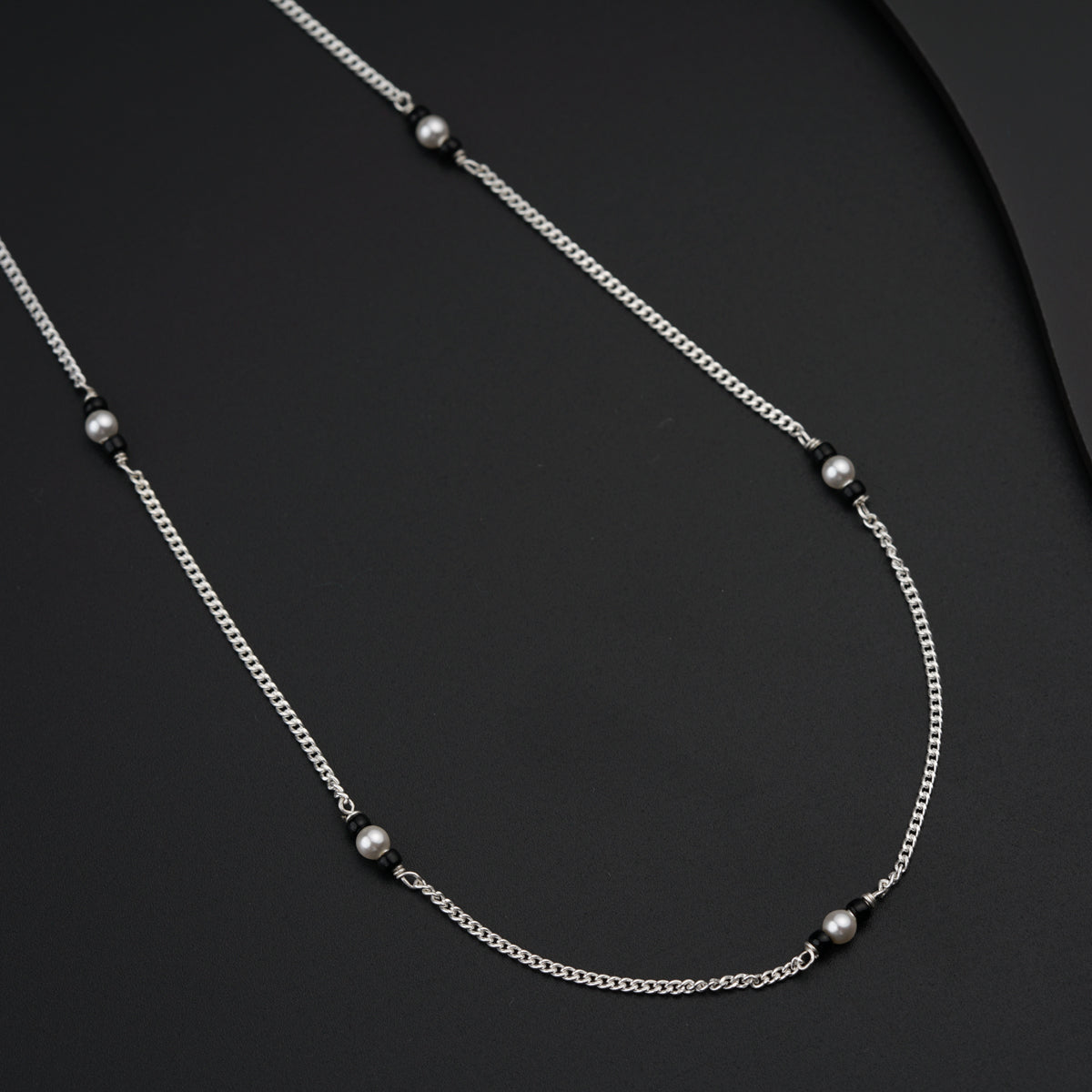 a silver necklace with pearls on a black surface