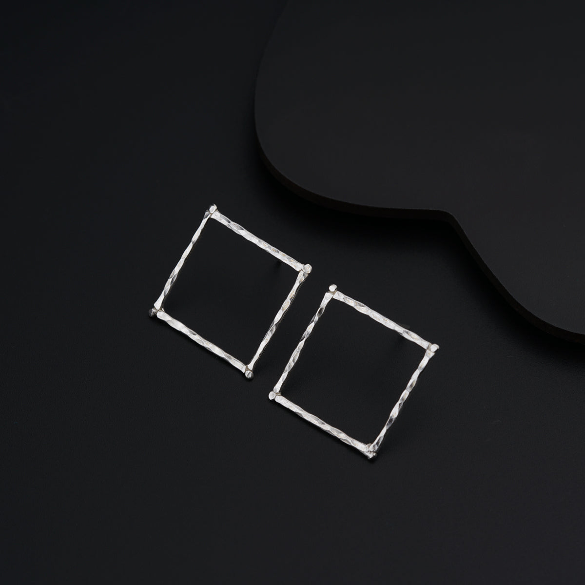 a pair of square earrings sitting on top of a black surface