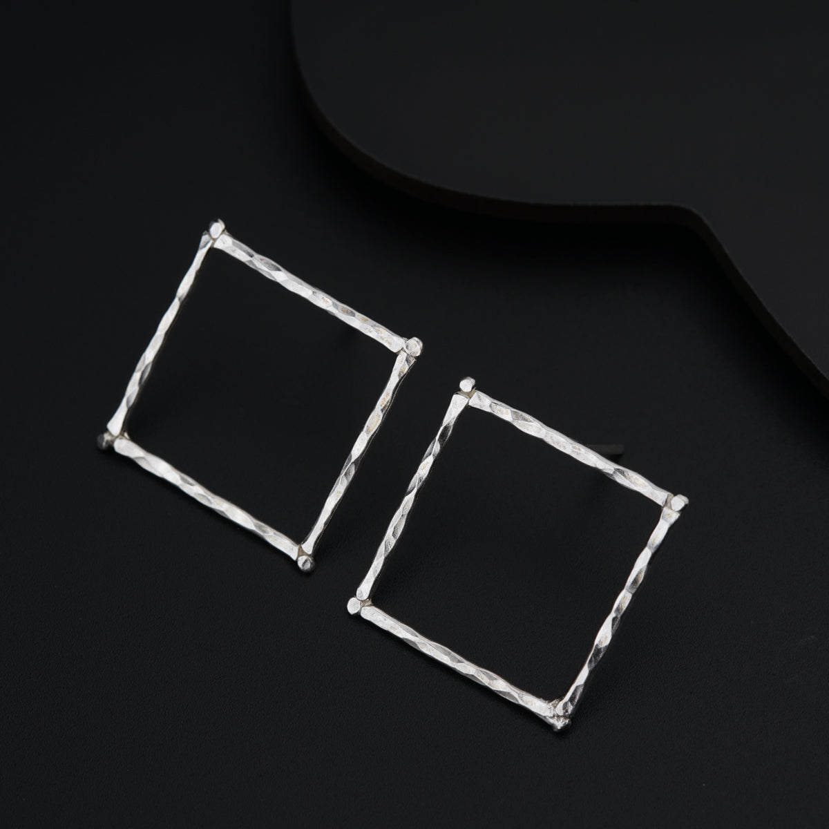 a pair of square earrings sitting on top of a black surface