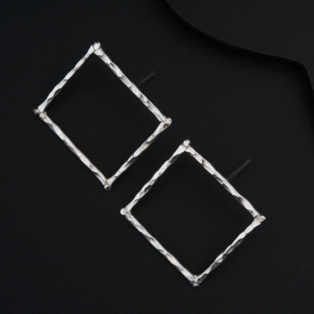 a pair of square shaped earrings sitting on top of a black surface