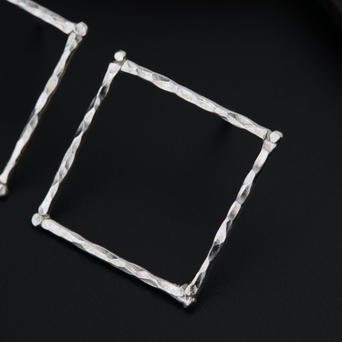 a pair of silver square earrings on a black surface