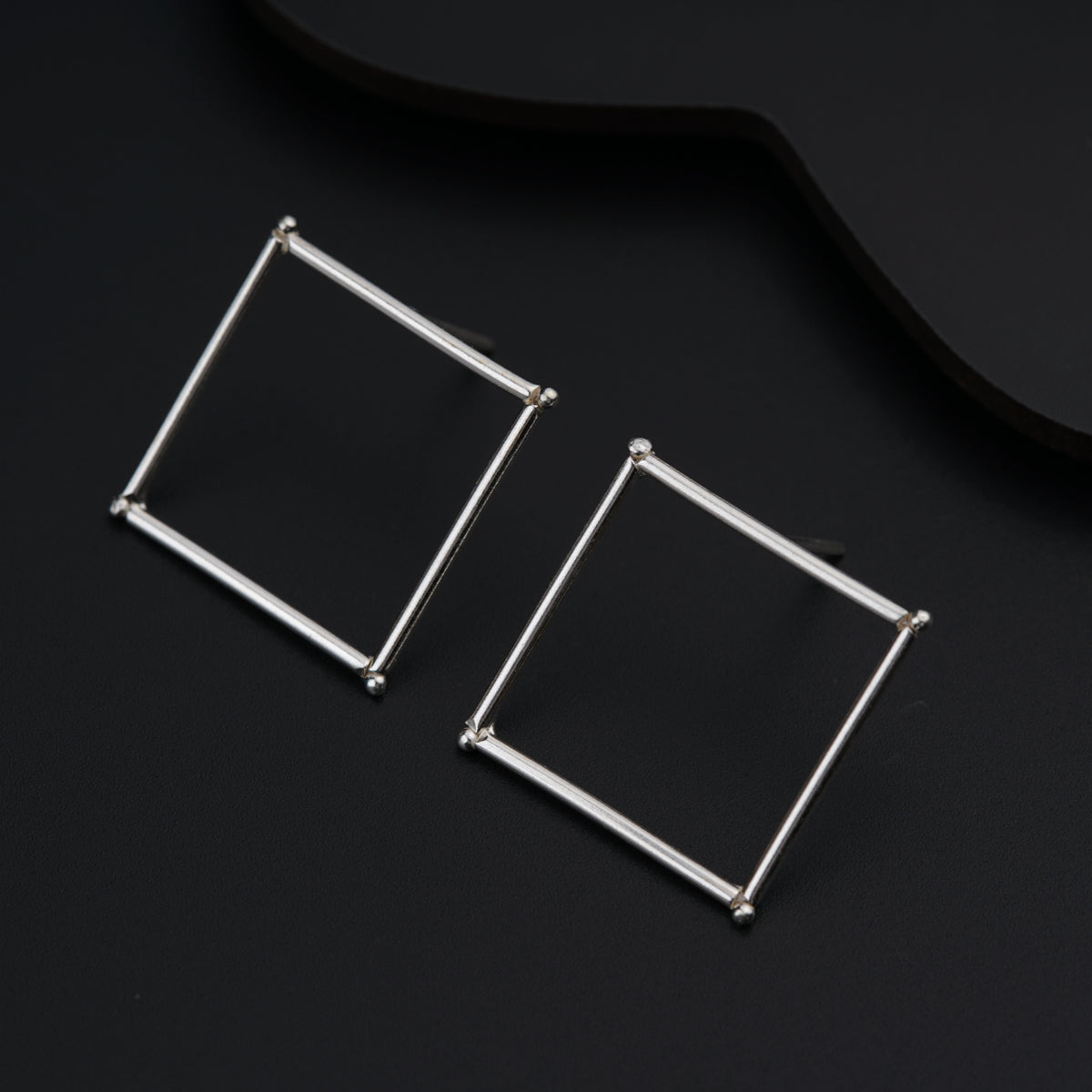 a pair of square earrings sitting on top of a black surface