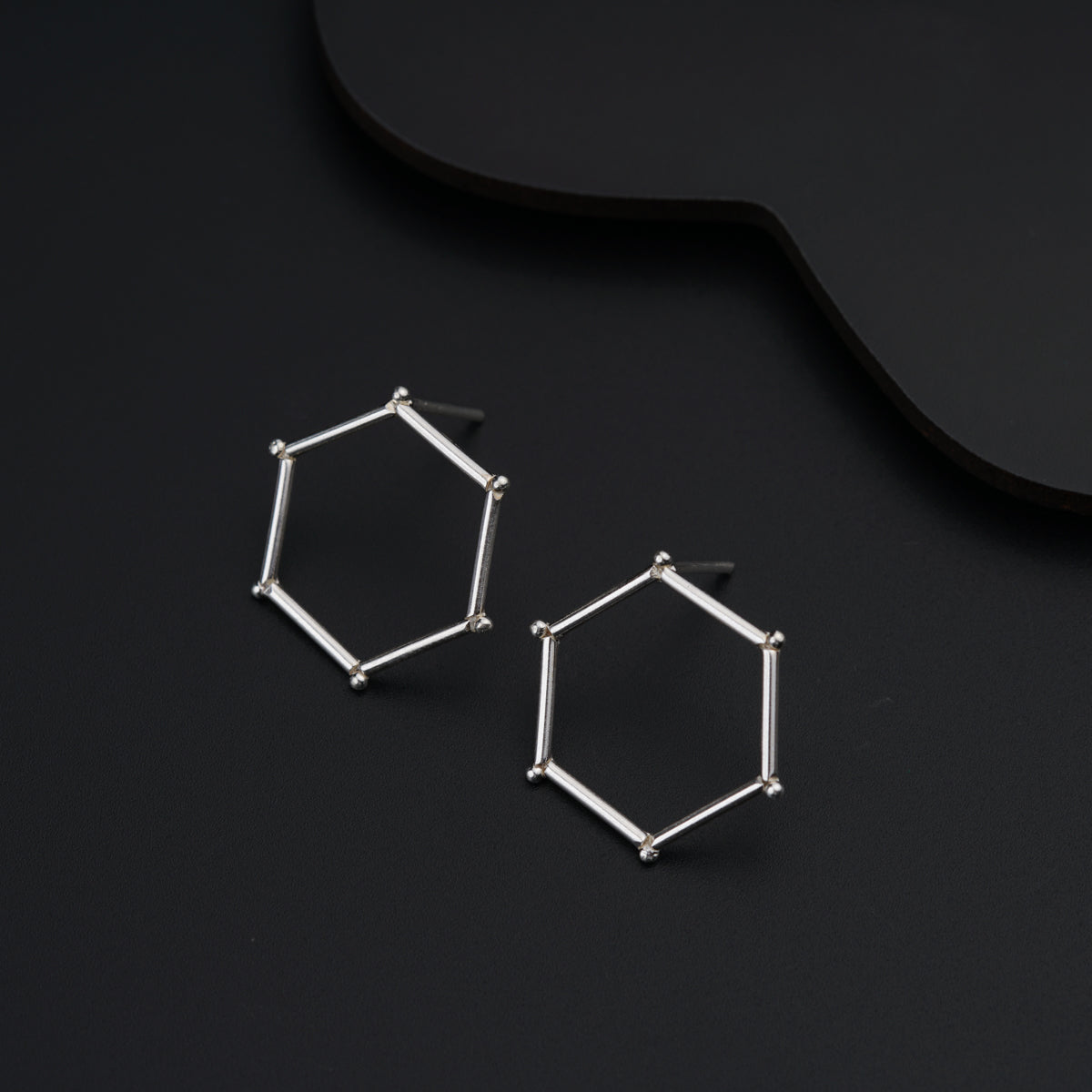 a pair of silver hexagonal earrings on a black surface