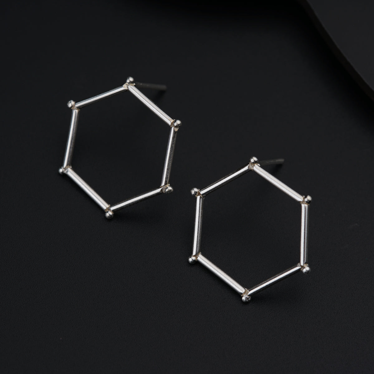 a pair of silver hexagonal earrings on a black surface