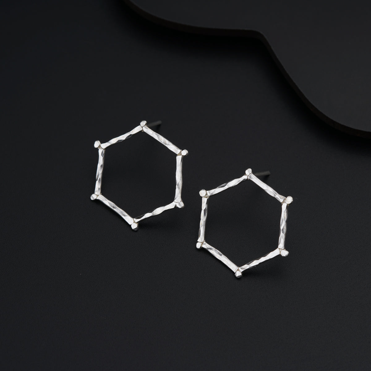 a pair of hexagonal earrings on a black surface