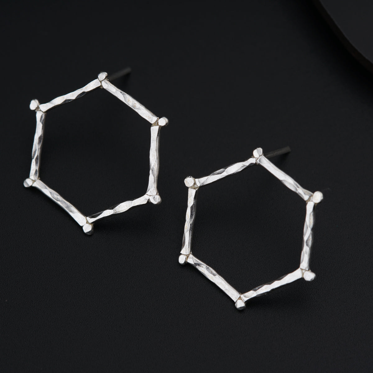 a pair of silver hexagonal earrings on a black surface