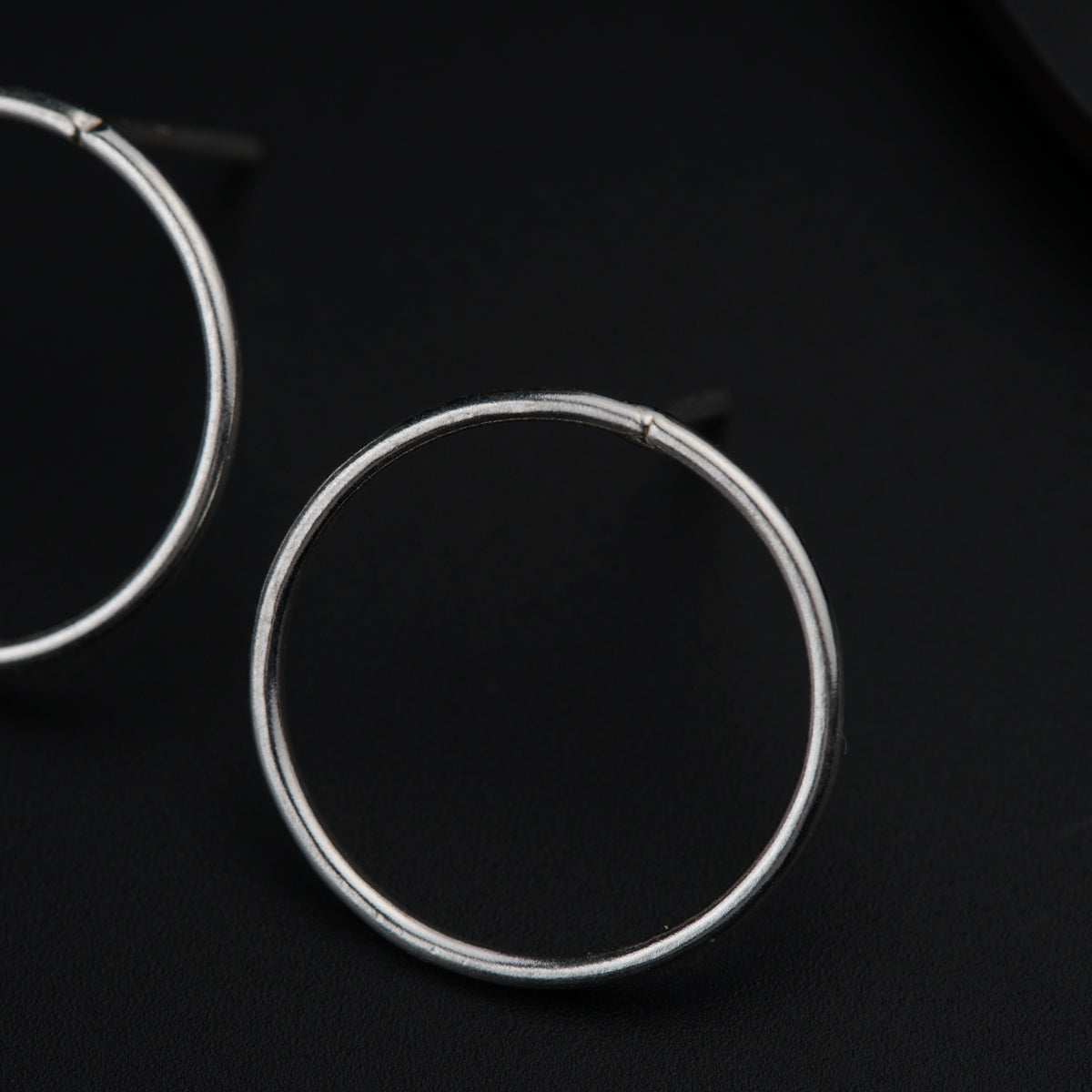 a pair of silver hoop earrings on a black surface
