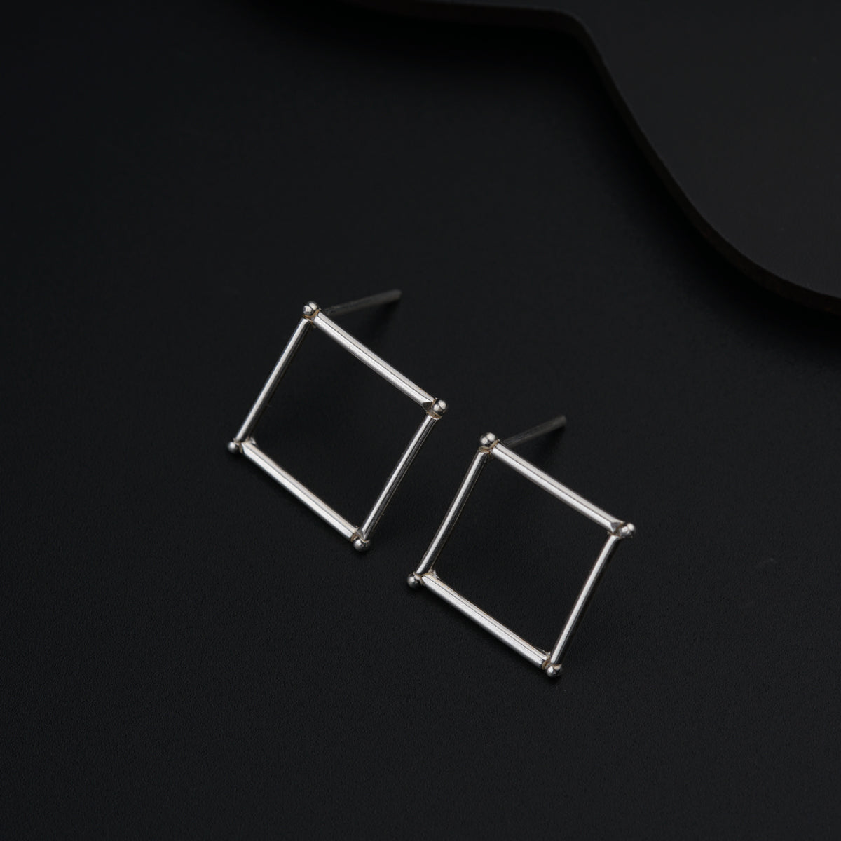 a pair of square earrings sitting on top of a black surface