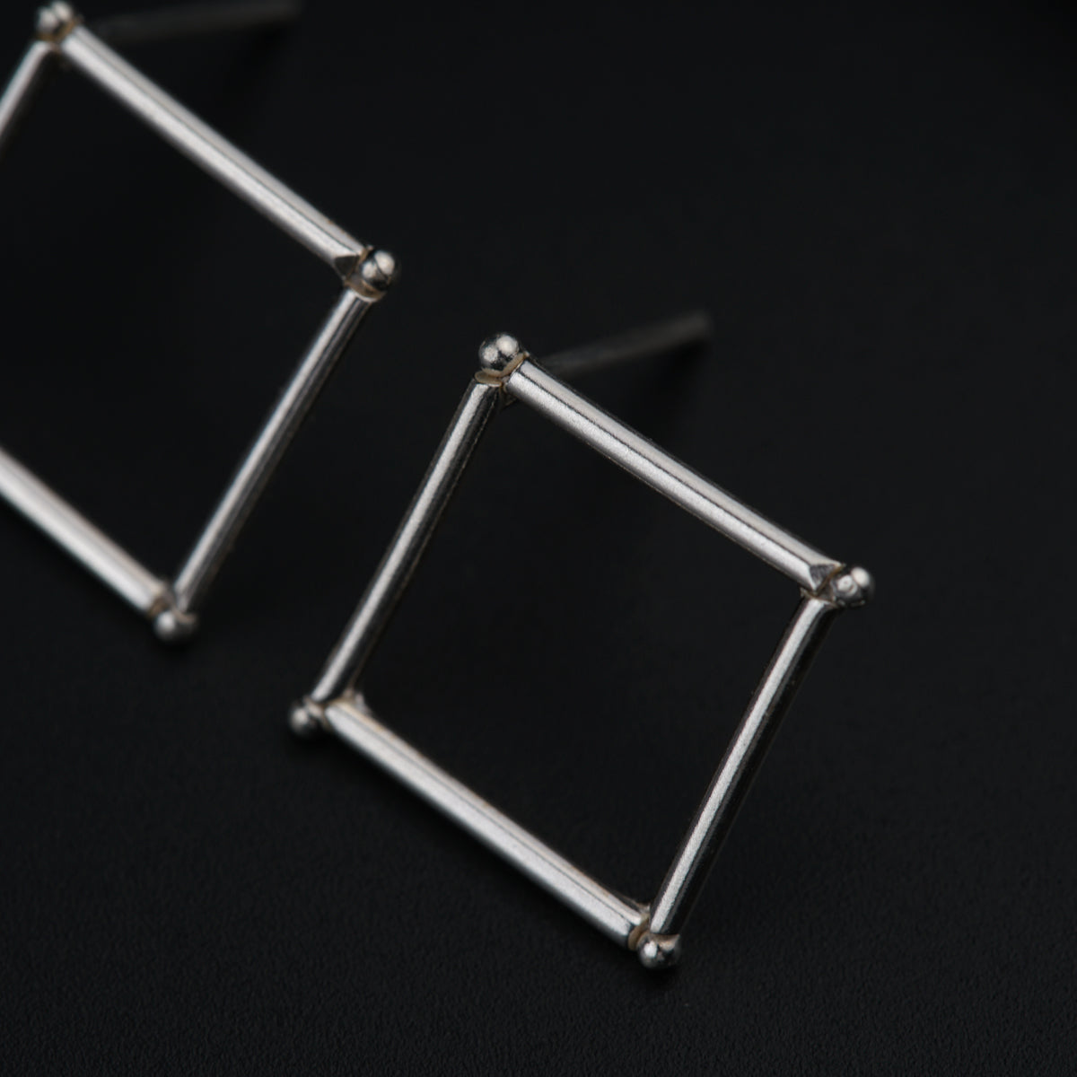 a pair of silver square earrings on a black surface