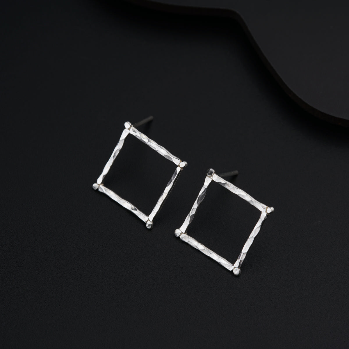 a pair of square earrings on a black surface