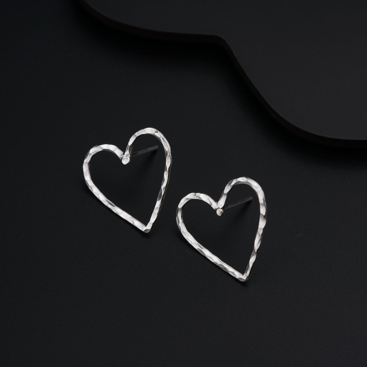 a pair of heart shaped earrings sitting on top of a black surface