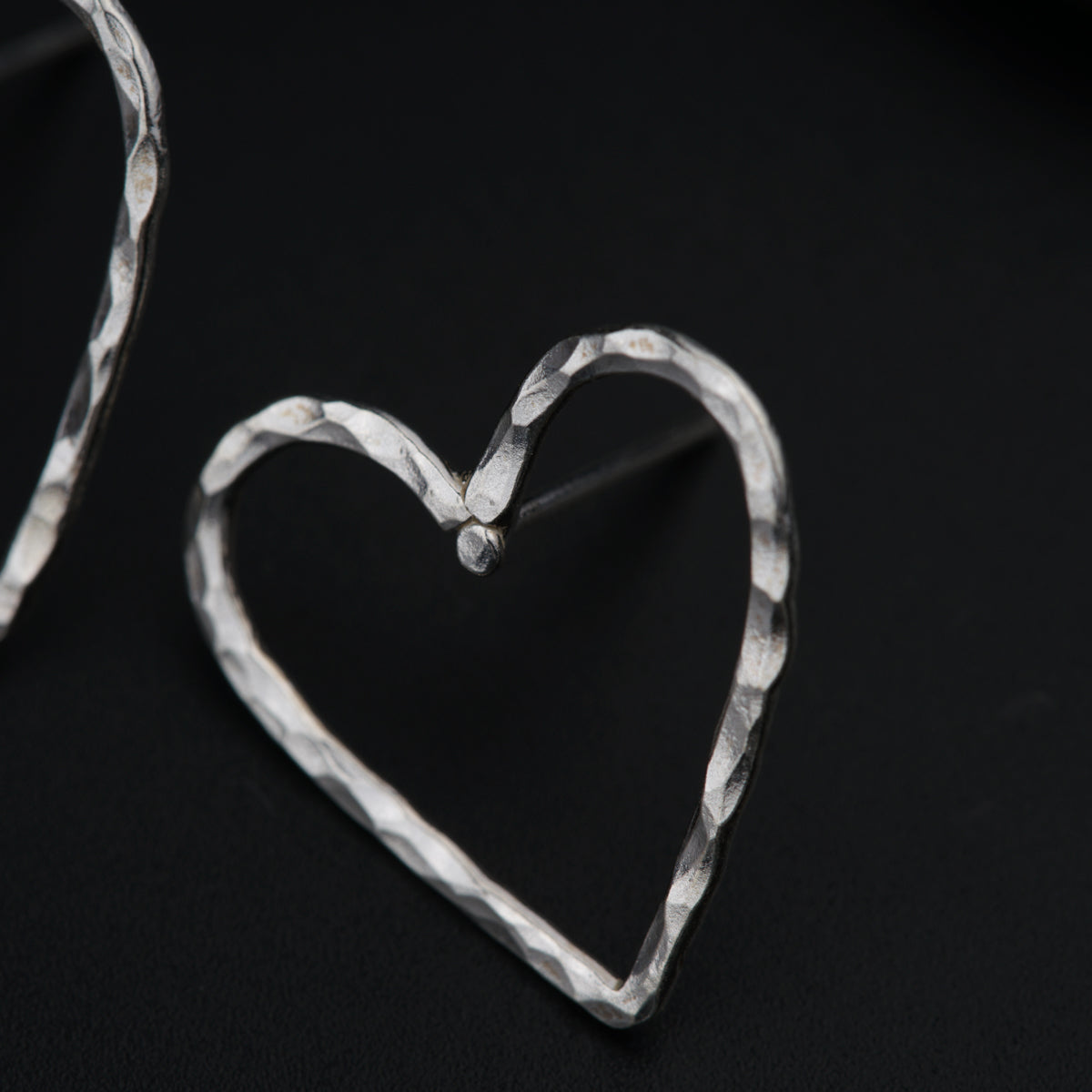 a pair of silver heart earrings on a black background