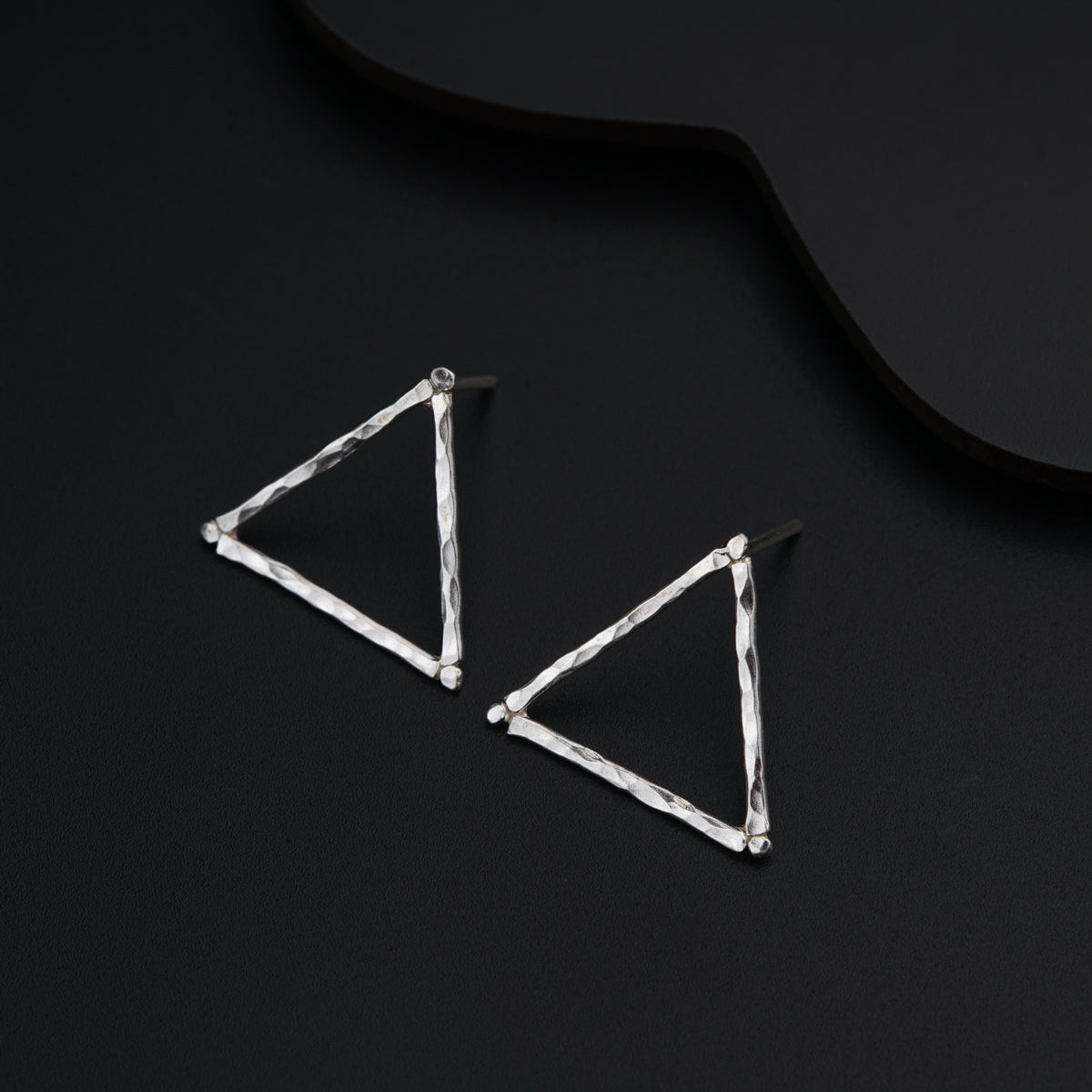 a pair of triangle shaped earrings on a black surface