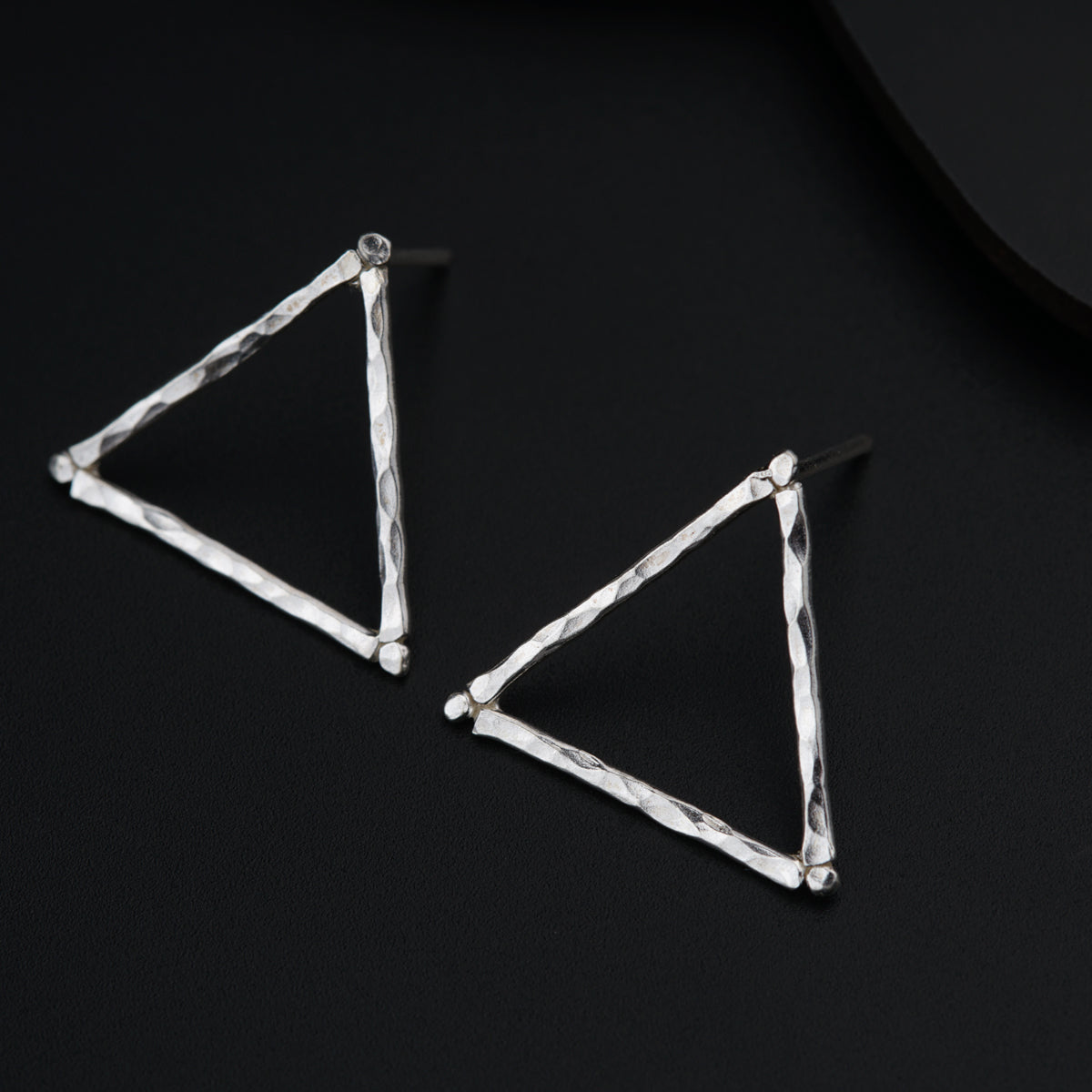 a pair of triangle shaped earrings on a black surface
