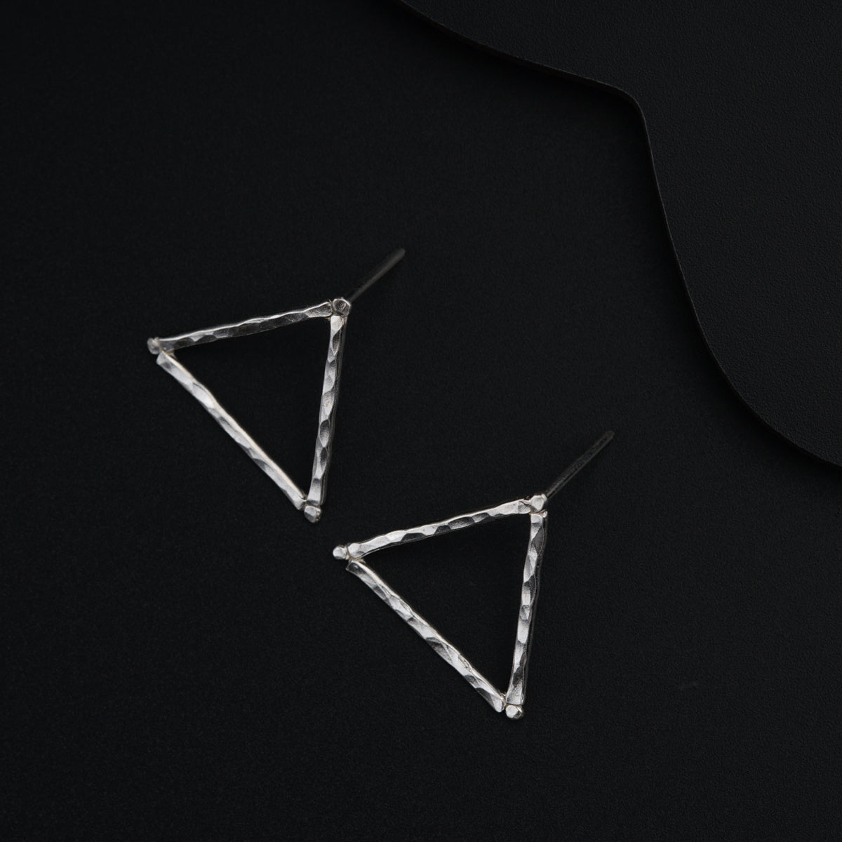 a pair of triangle shaped earrings sitting on top of a black surface