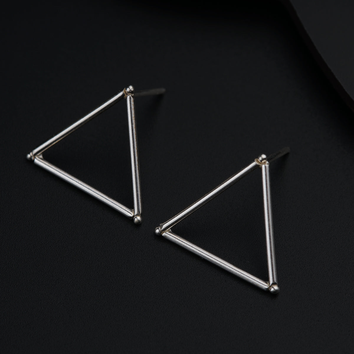 a pair of triangle earrings on a black surface