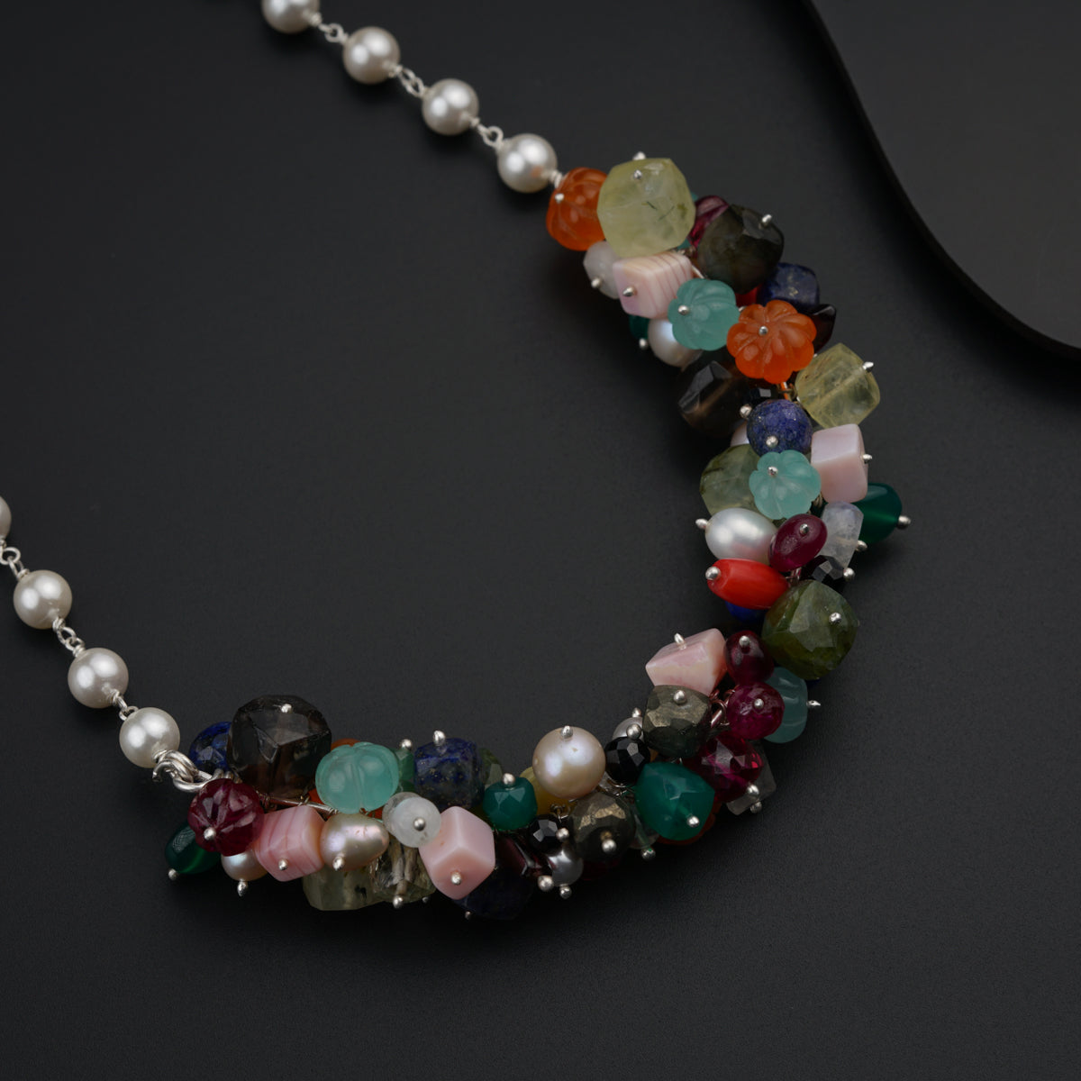 a multi - colored beaded necklace with pearls on a black surface
