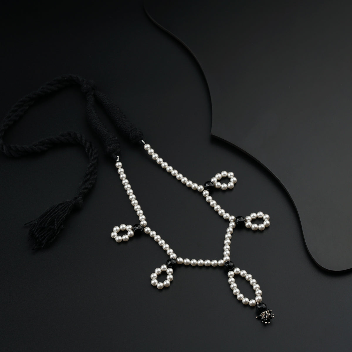 a necklace with pearls and a tassel on a black surface
