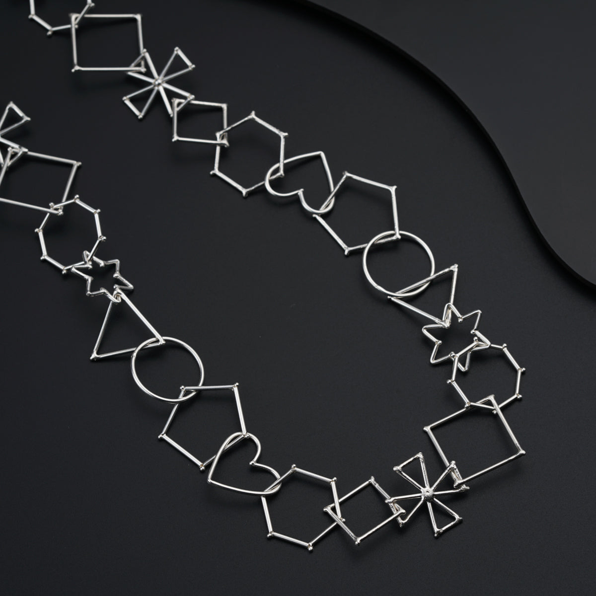 a silver necklace with geometric shapes on a black surface