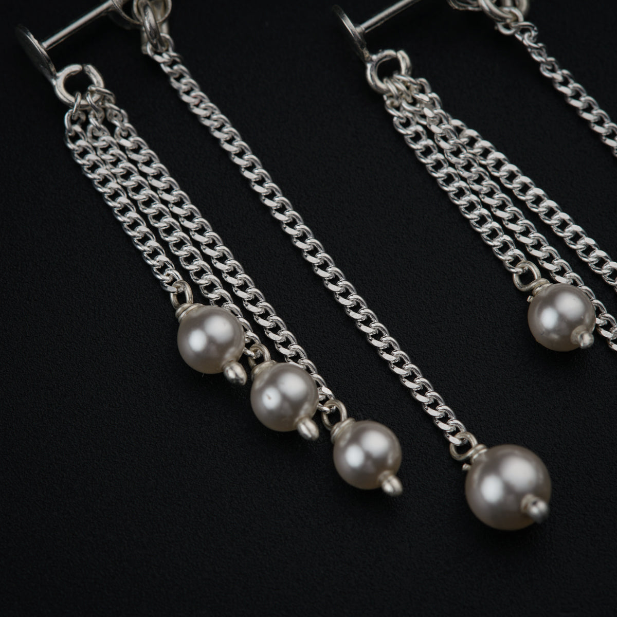 a pair of earrings with pearls hanging from chains