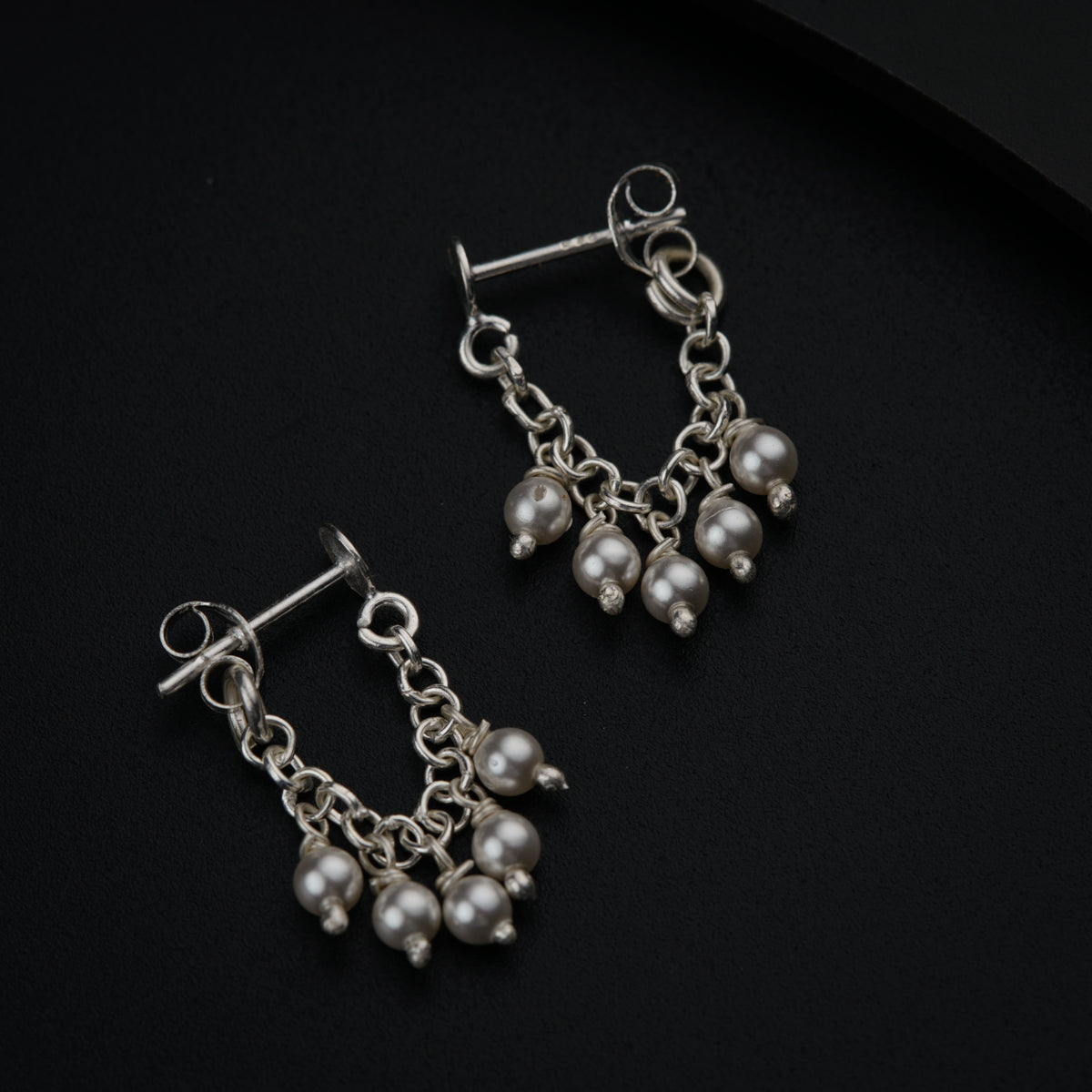 a pair of dangling earrings on a black surface