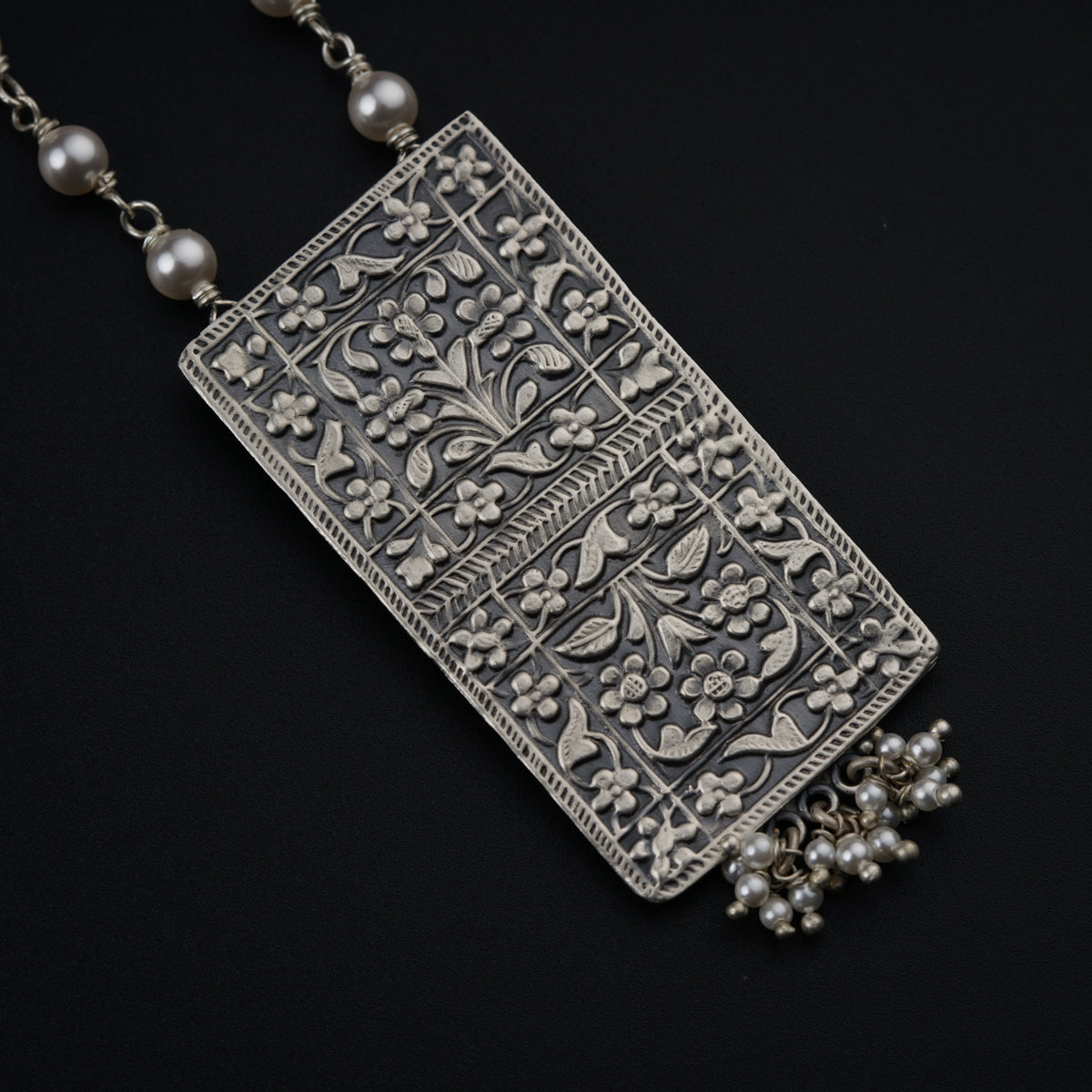 a silver necklace with pearls on a black background