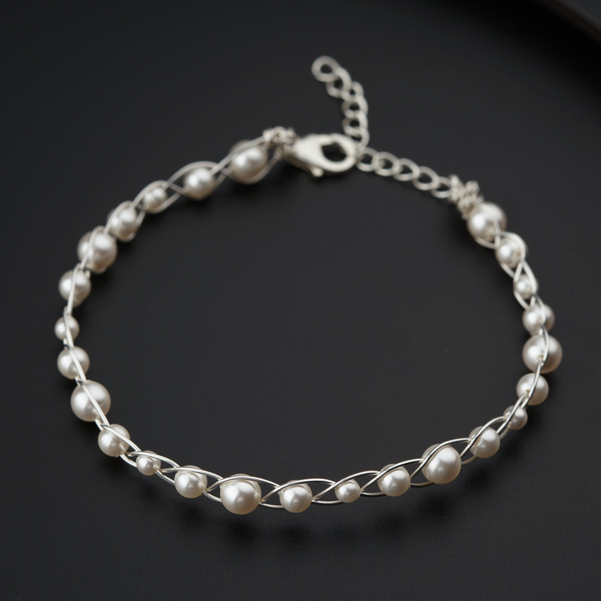 a silver bracelet with pearls on a black surface