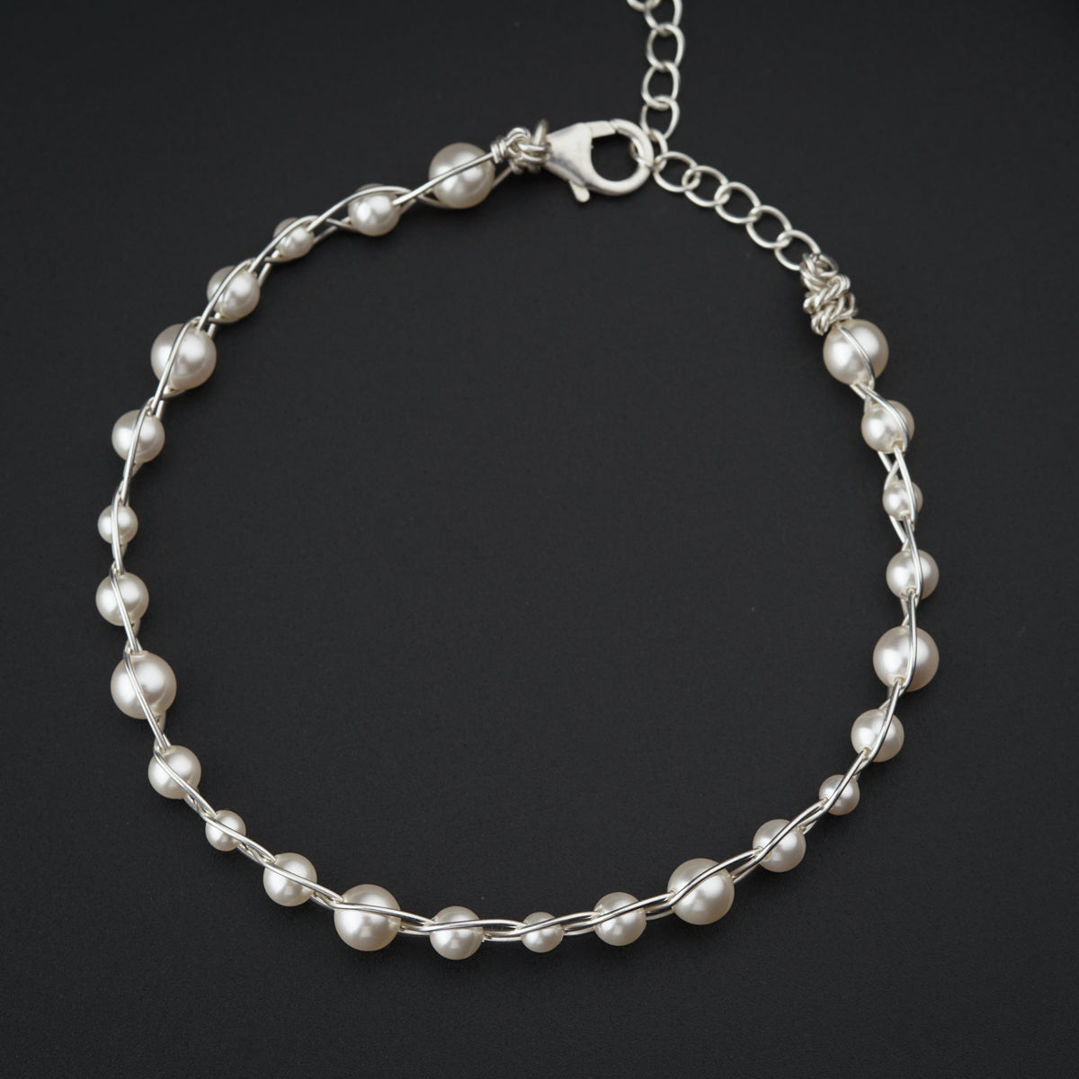 a silver bracelet with pearls on a black background