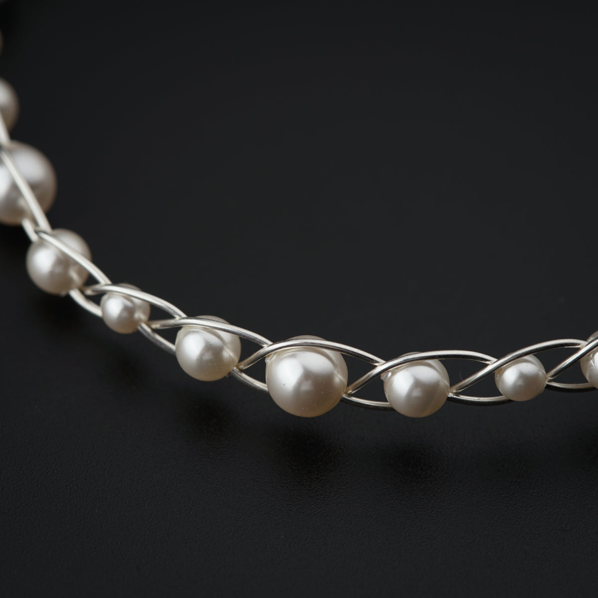 a silver necklace with pearls on a black background