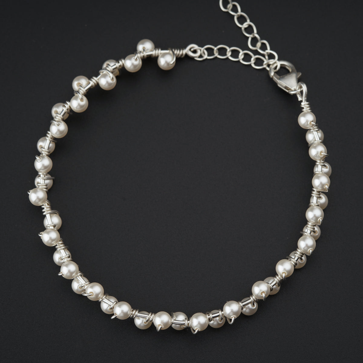 a silver bracelet with pearls on a black background