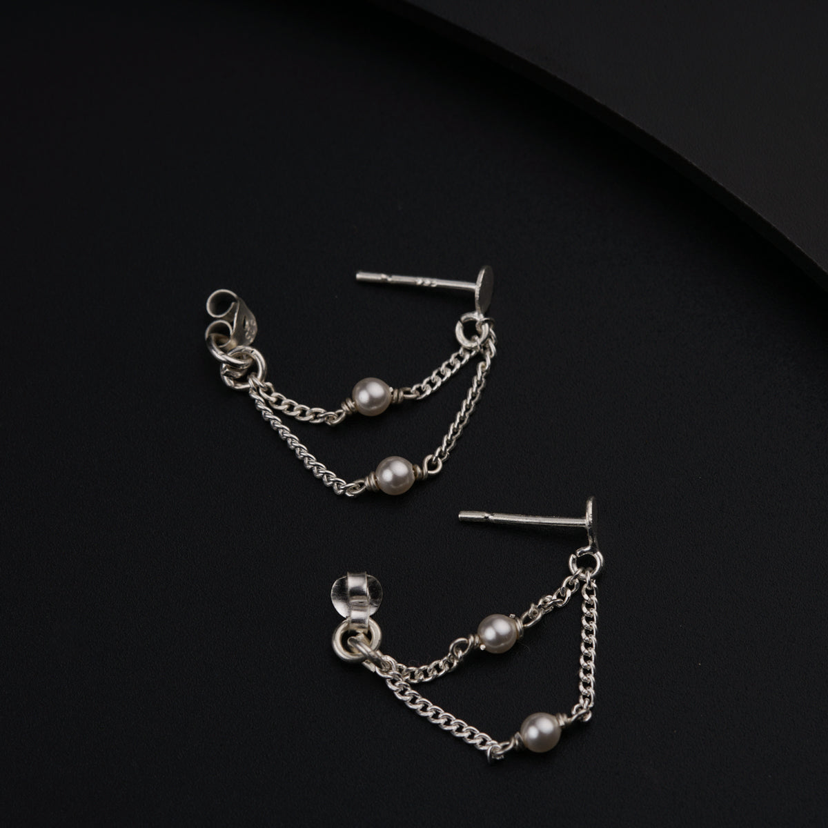 a pair of chain and pearl earrings on a black surface