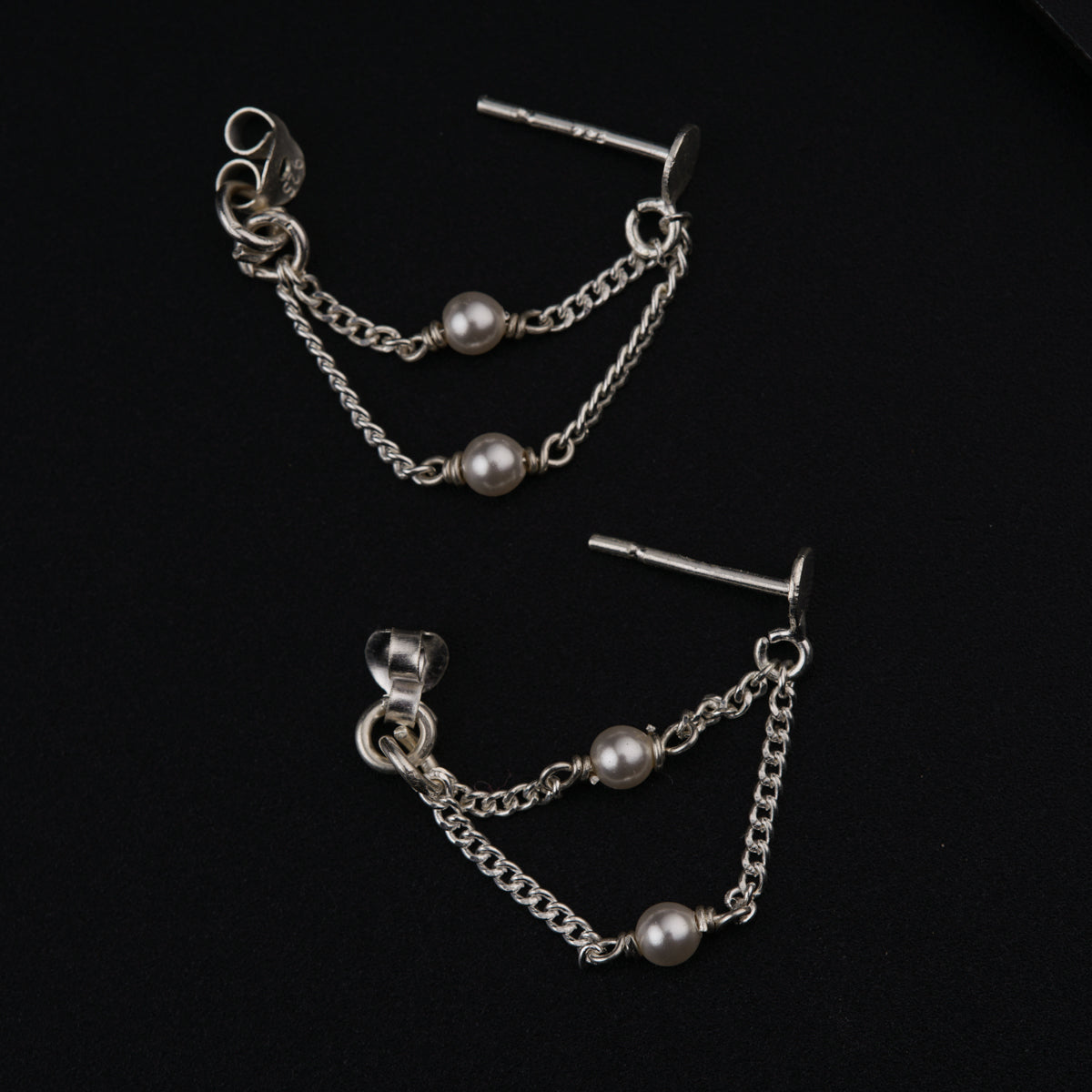 a pair of chain and pearl earrings on a black background