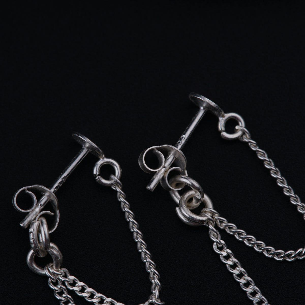 a pair of silver earrings with chains on a black background