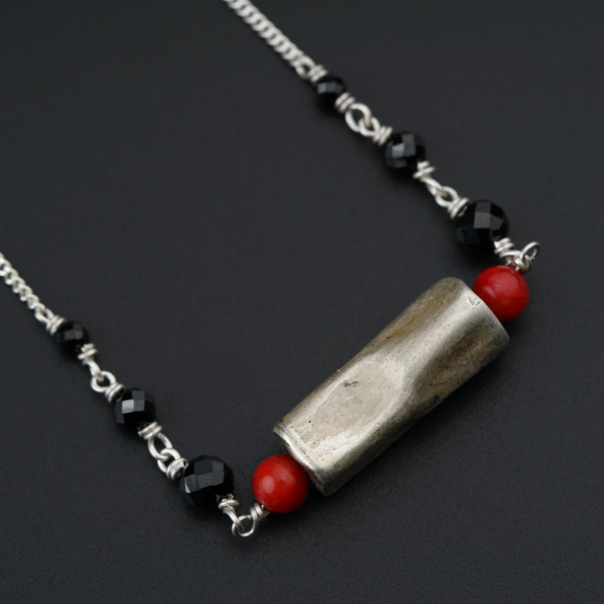 a silver and red necklace on a black surface