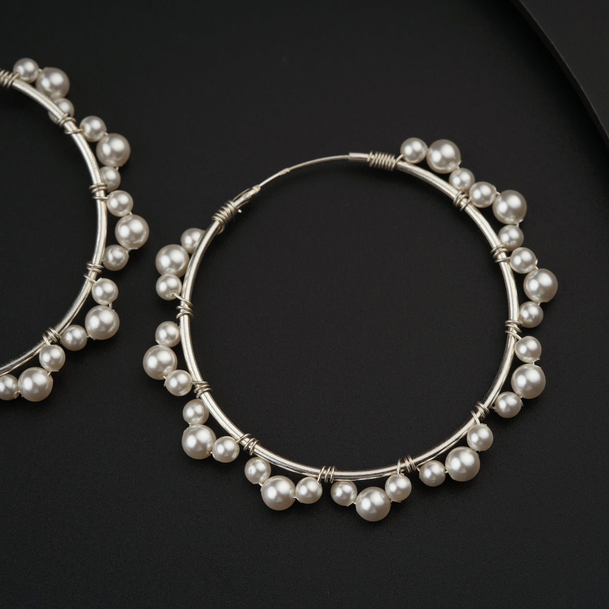 a pair of hoop earrings with pearls on a black surface