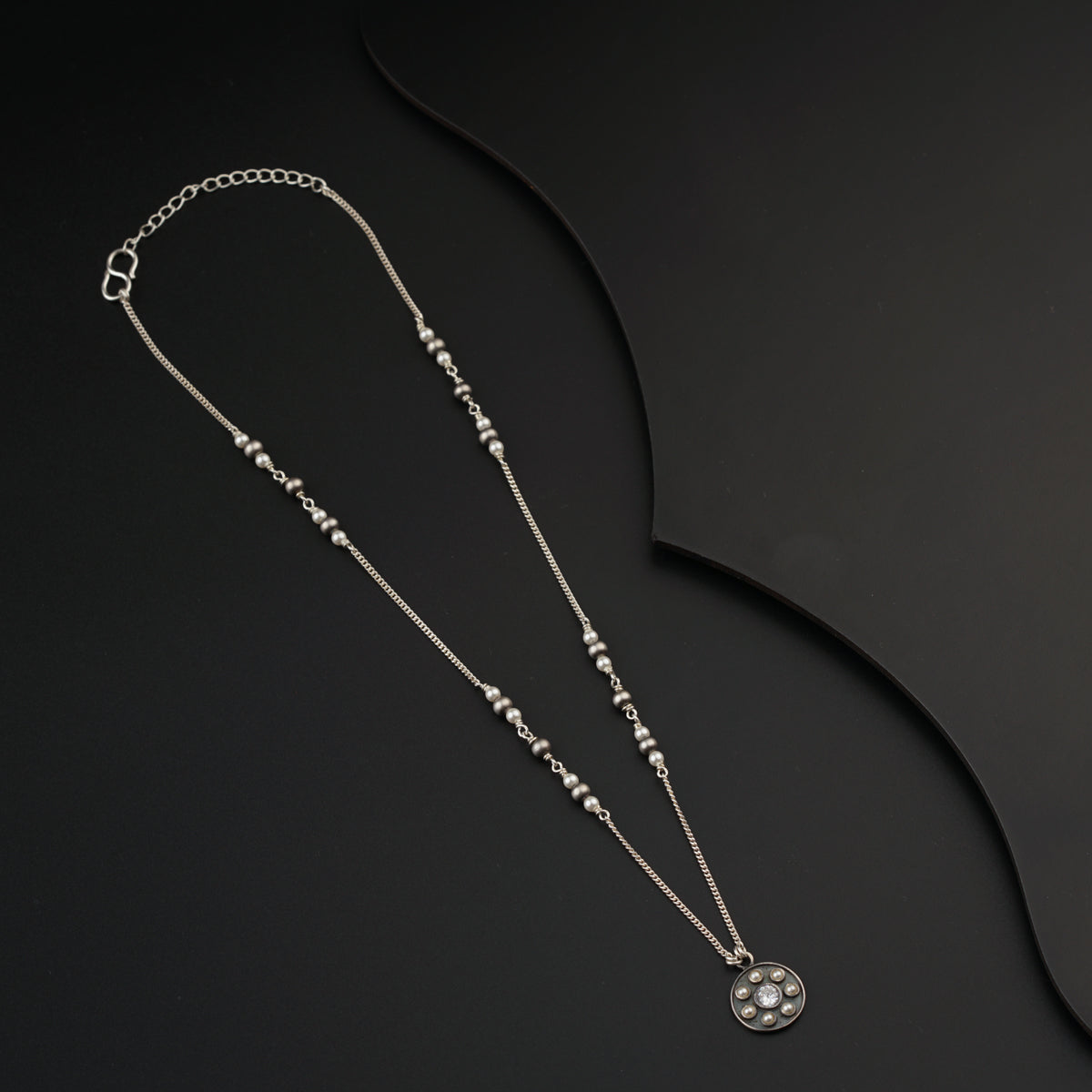 a silver necklace with a diamond on a black background