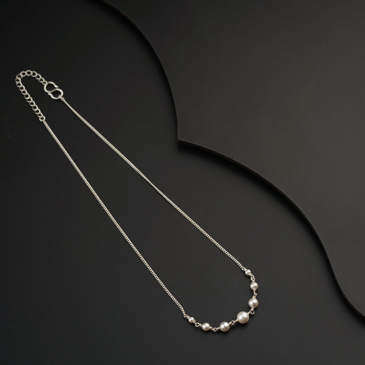 a silver necklace with pearls on a black background
