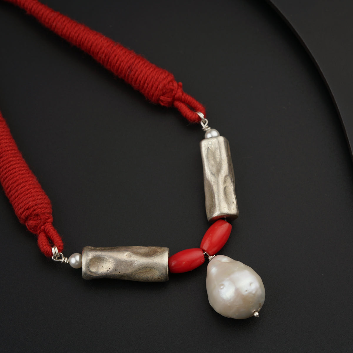 a red and silver necklace with a white pearl