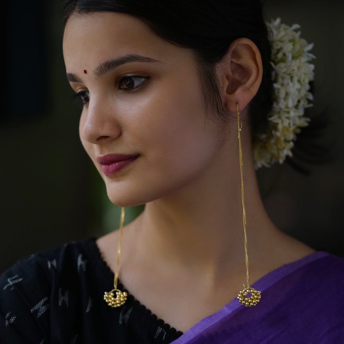 a woman wearing a purple saree and gold earrings