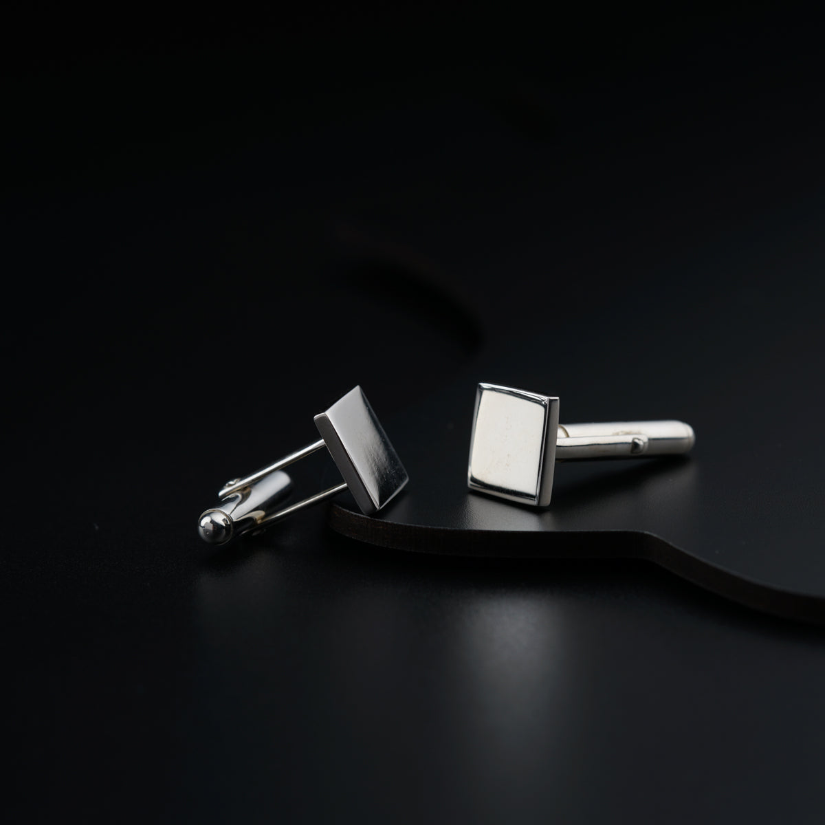 a pair of silver cufflinkes on a black surface