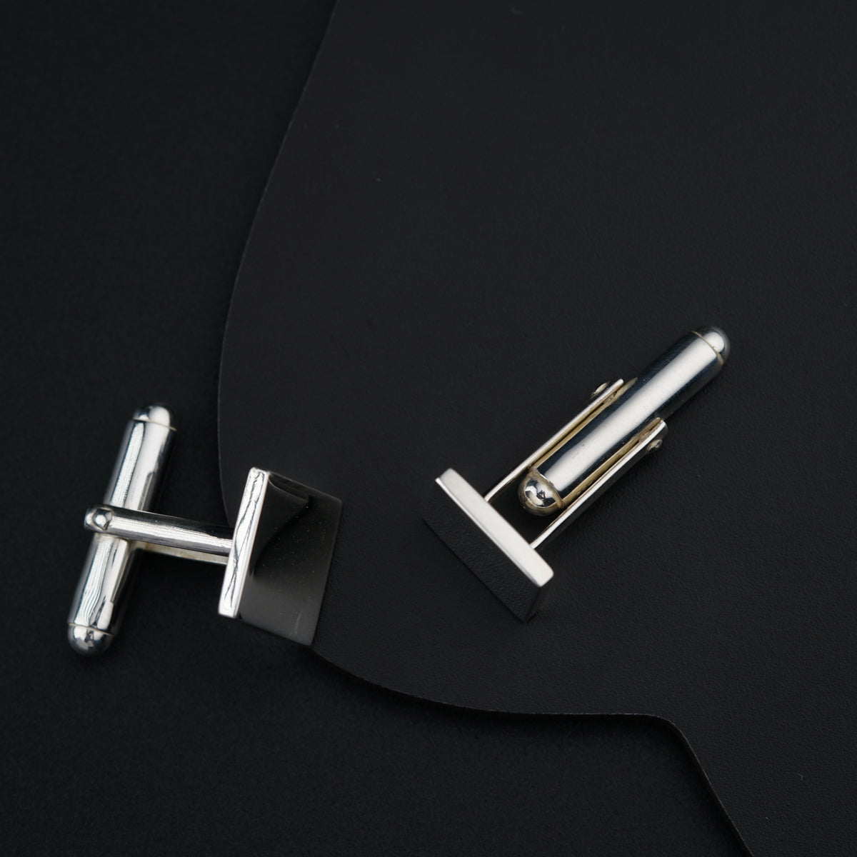 a pair of silver cufflinks sitting on top of a black piece of paper
