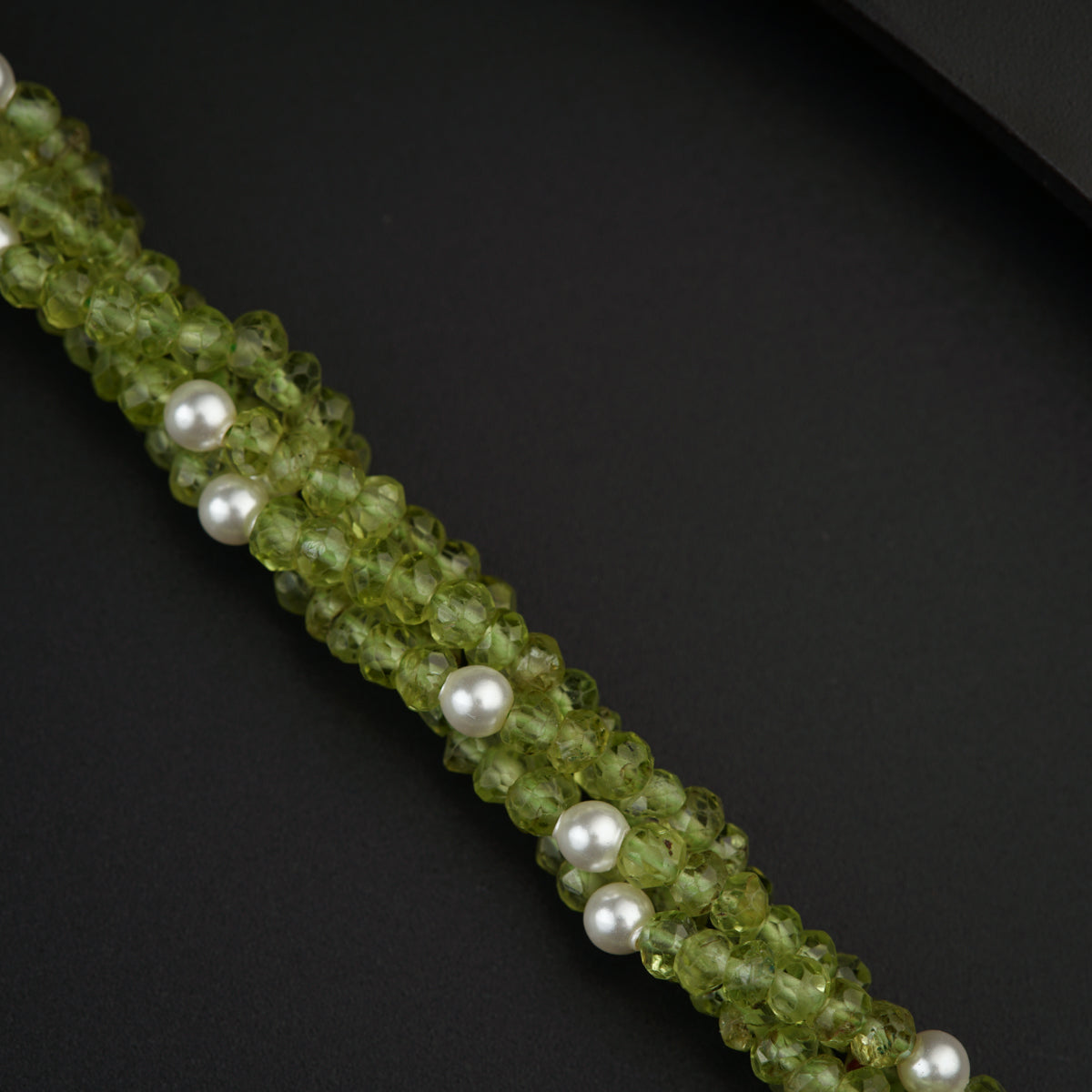 a green beaded bracelet with pearls on a black background