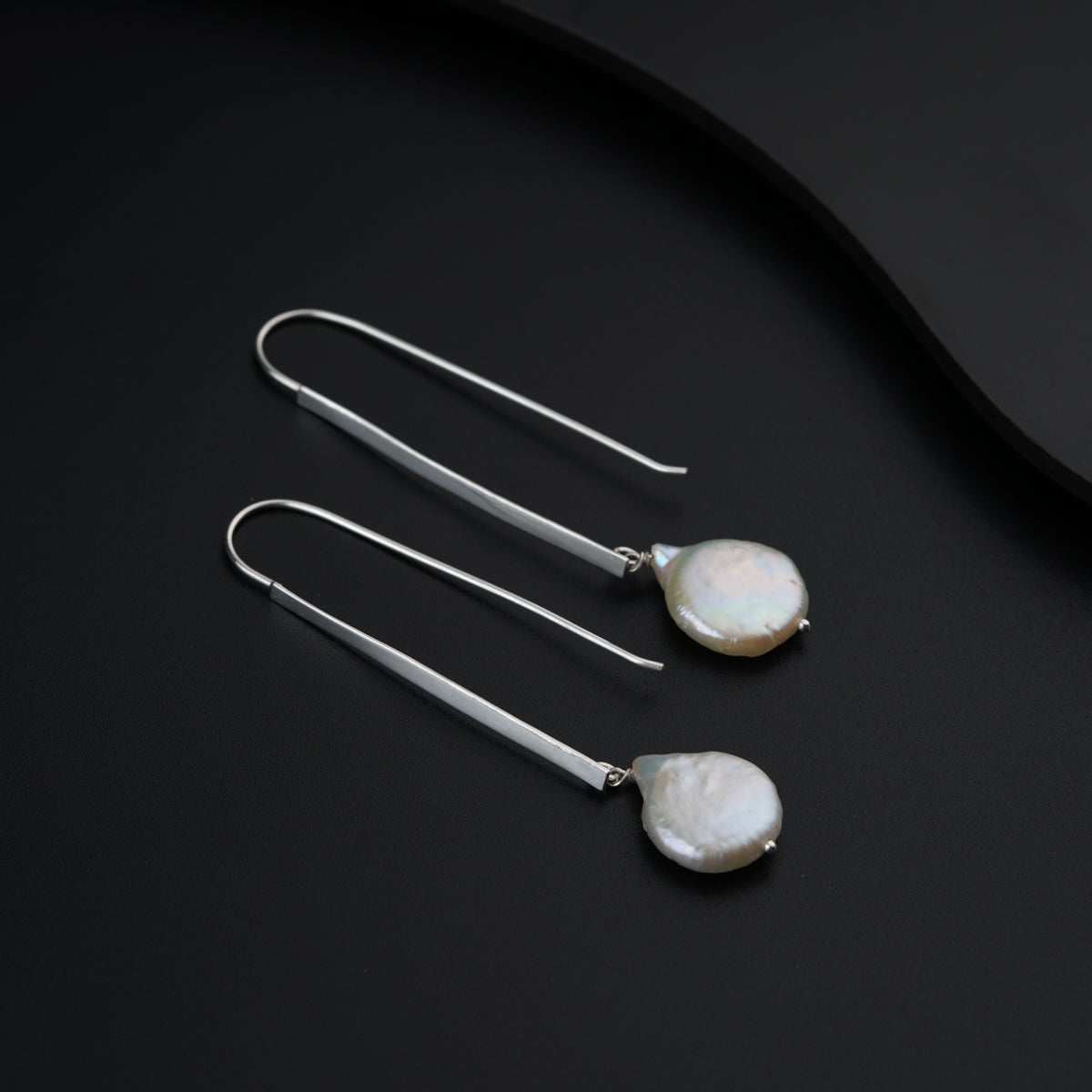 a pair of earrings with white pearls on a black surface
