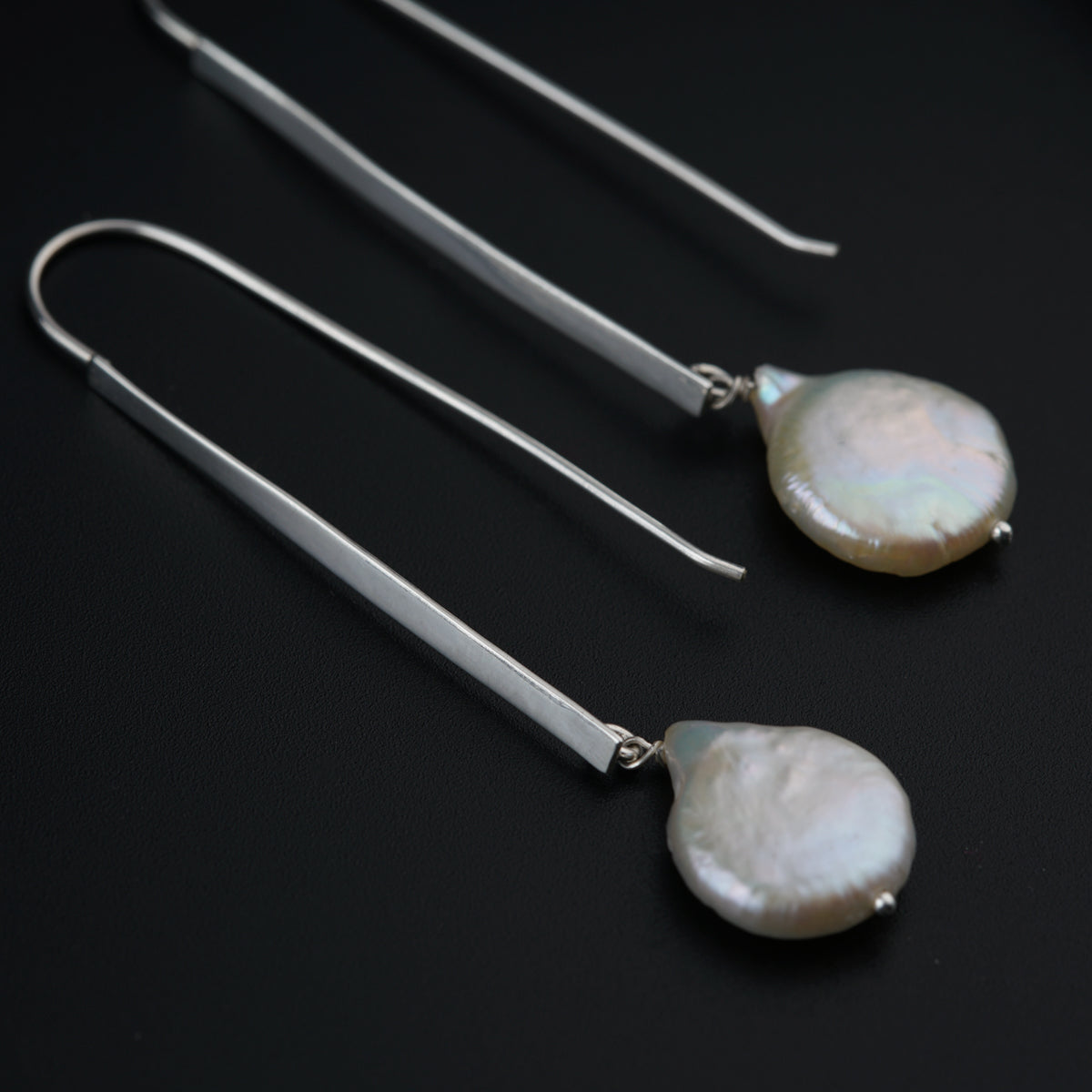 a pair of earrings with a white pearl hanging from them
