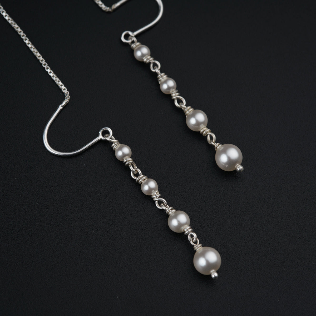 a pair of earrings with pearls hanging from a chain