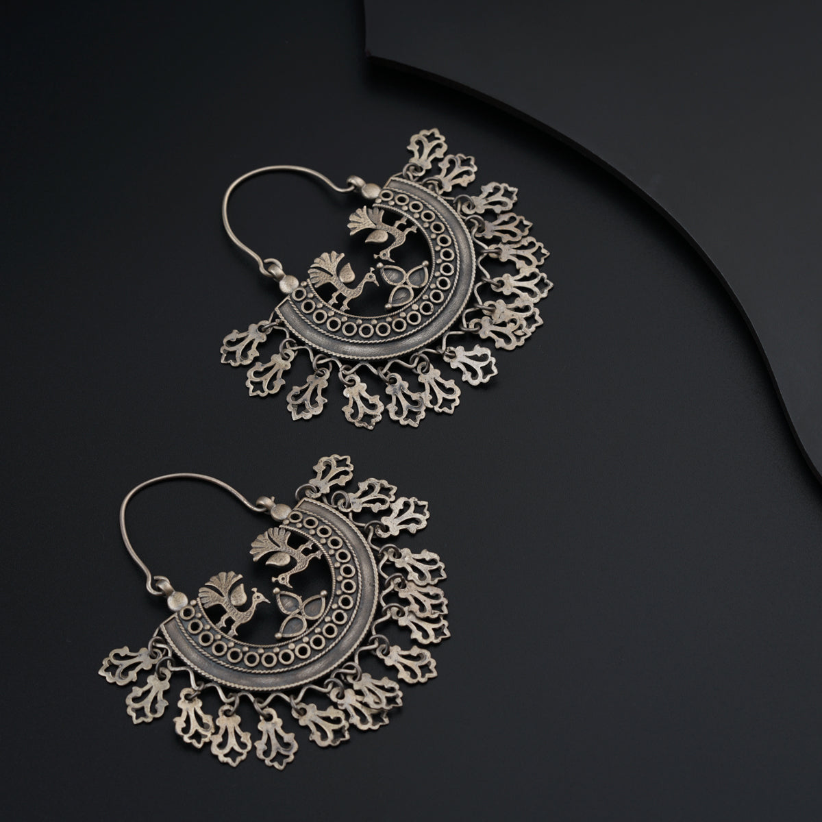 a pair of silver toned earrings on a black background