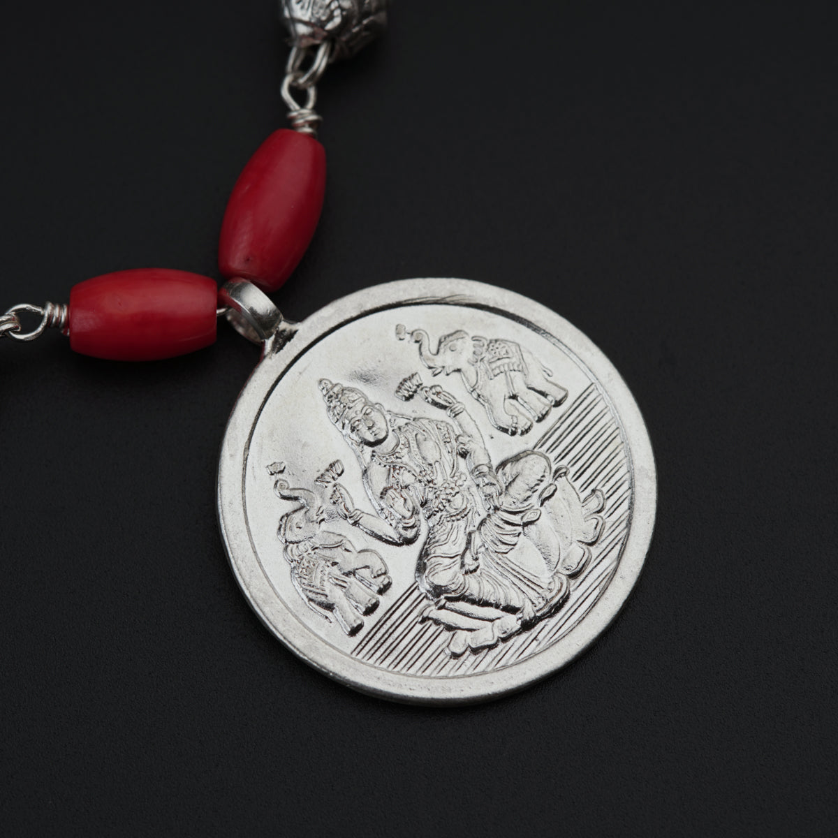 a red beaded necklace with a silver coin on it